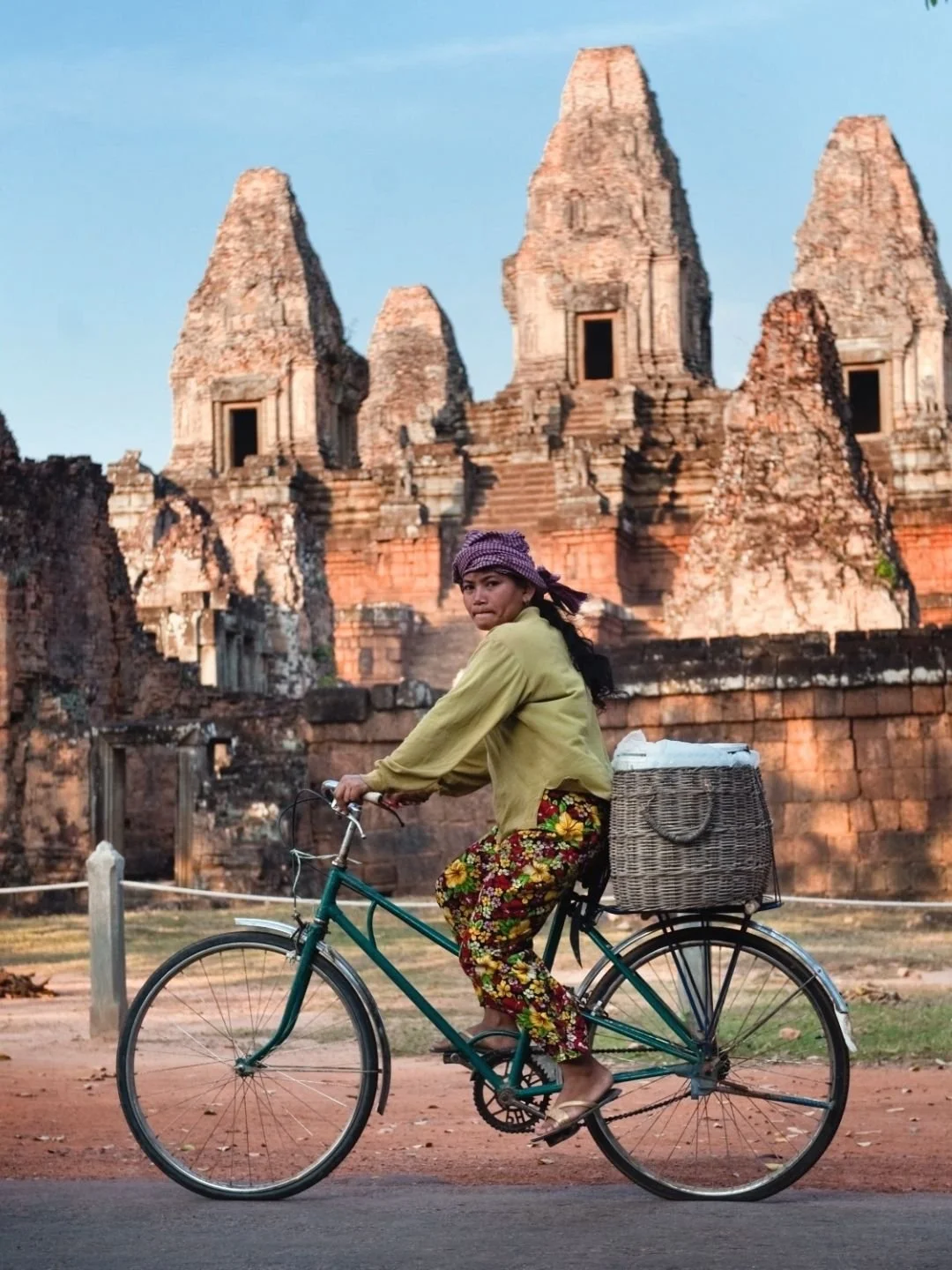Local woman riding a bicycle past ancient sandstone temple ruins in the Angkor archaeological complex, Cambodia.