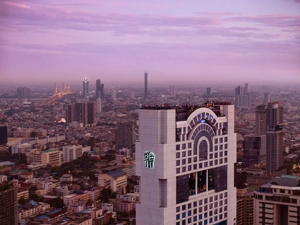 A city skyline during sunset with tall buildings and a large clock tower in the foreground.