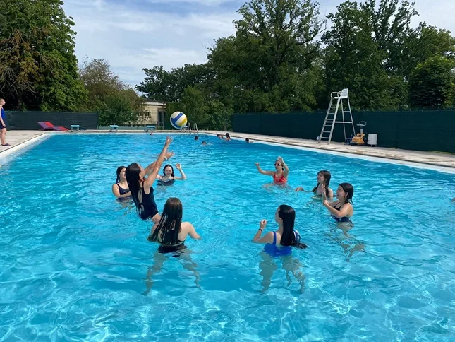 Group of young women playing volleyball in a swimming pool outdoors on a sunny day.