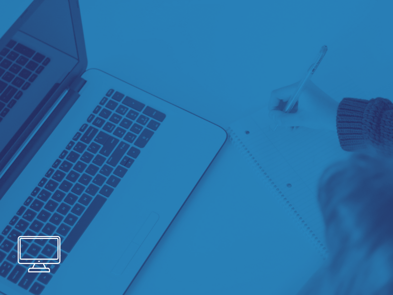 Open laptop computer with a keyboard and screen visible, a person's hand writing in a notebook with a pen on a table.