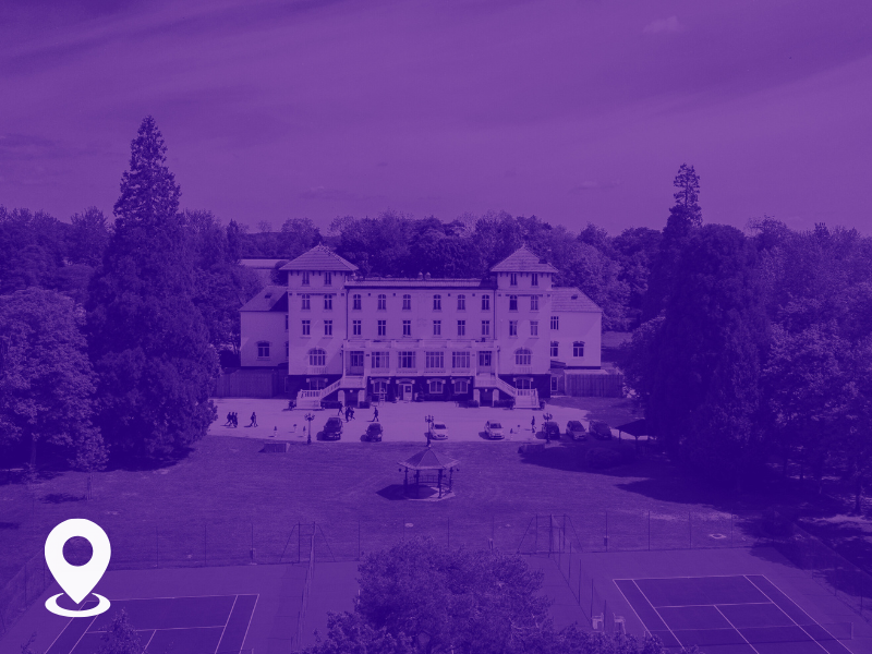 A large, multi-story building with a central tower, surrounded by trees, with a parking lot and tennis courts in the foreground.