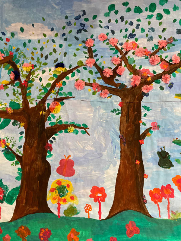 Colorful children's drawing of two large trees with pink blossoms, surrounded by various animals and plants, set against a blue sky.