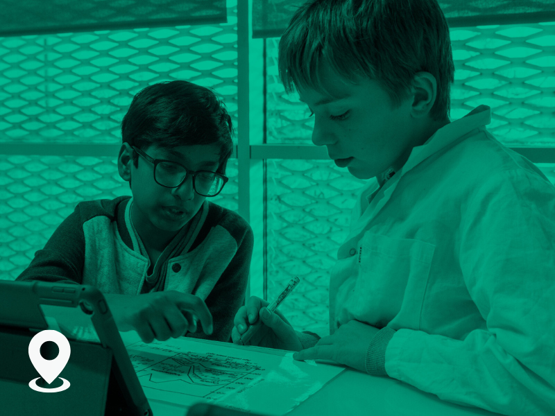 Two young students working together on a school assignment or project at a table in a brightly lit room.