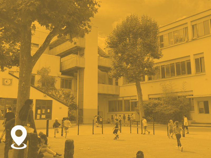 Children playing in a courtyard surrounded by modern school buildings with trees.