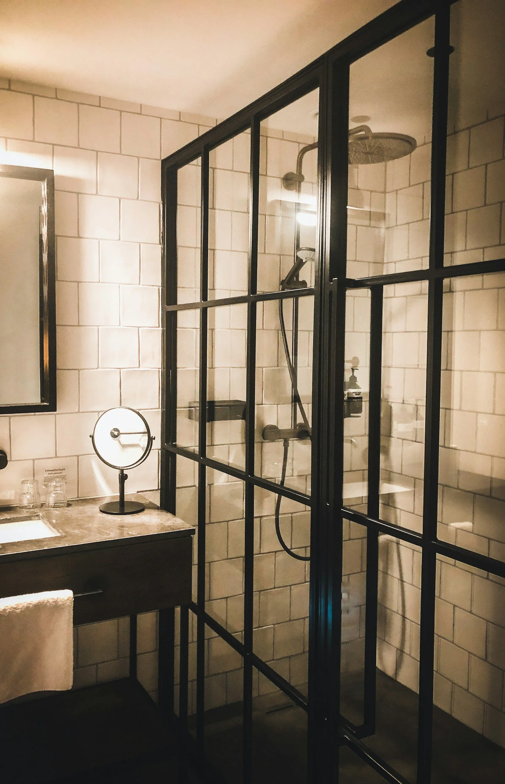 A modern bathroom with a glass-enclosed shower, beige tiled walls, a mirror, a vanity with a marble countertop, and a towel.