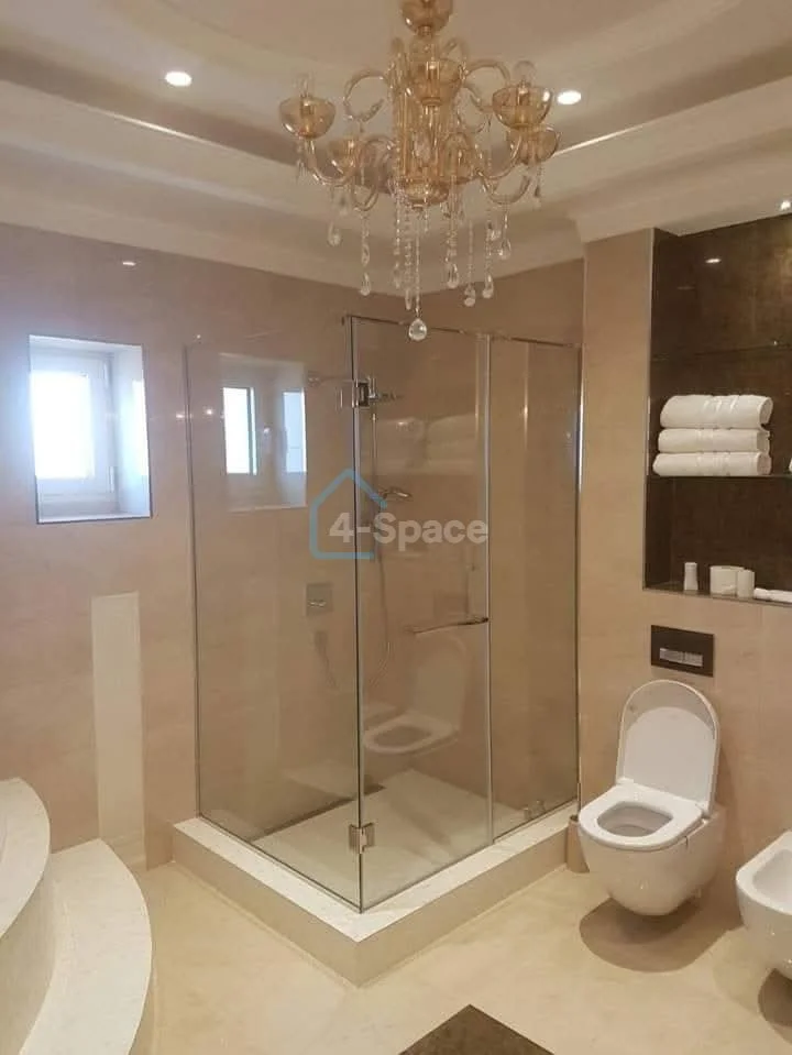 Bathroom with a glass shower enclosure, a toilet with an open lid, and a chandelier hanging from the ceiling.