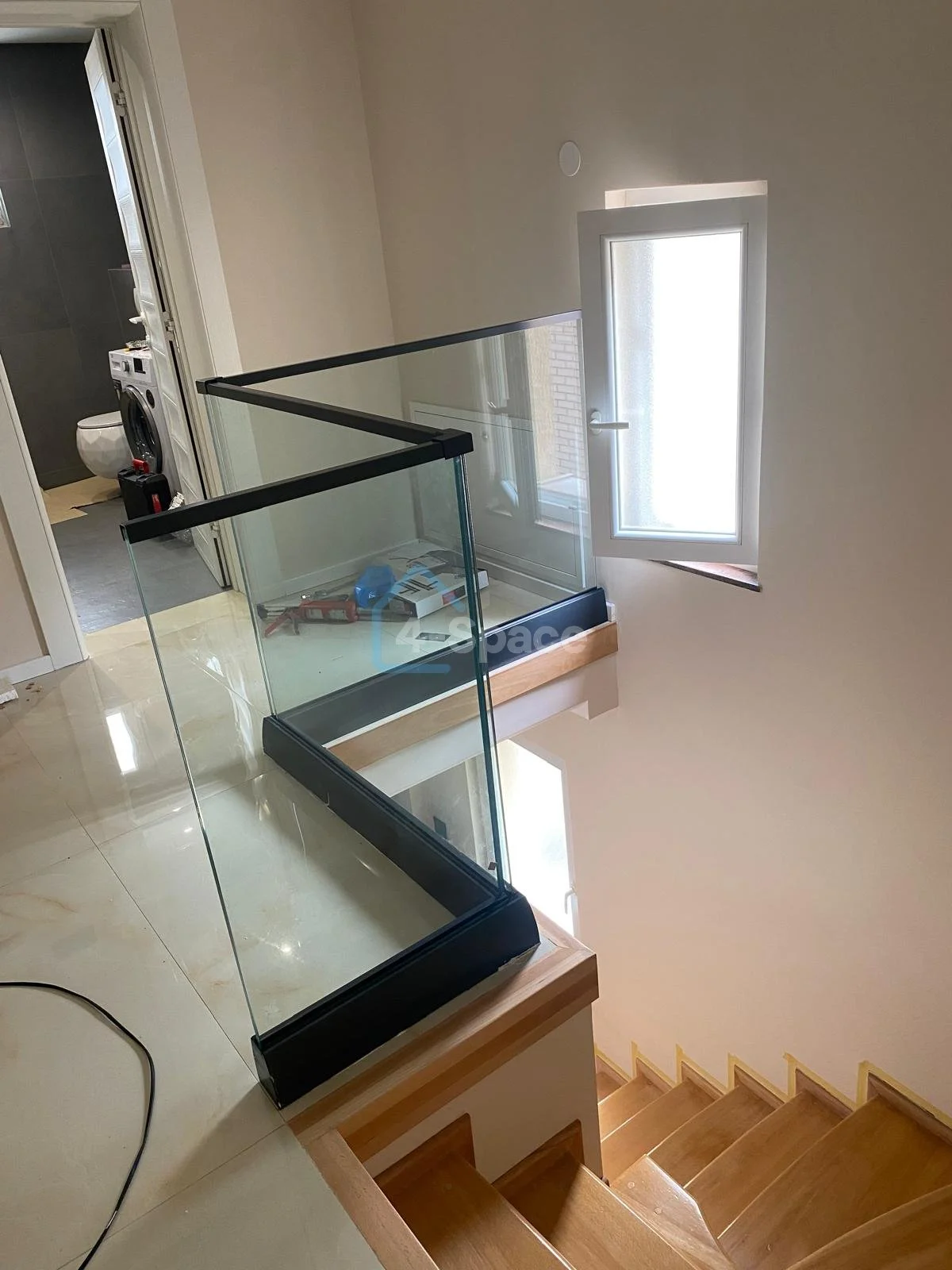 A glass display case on a wooden platform overlooking a staircase in a bright, modern room, with a window on the adjacent wall.