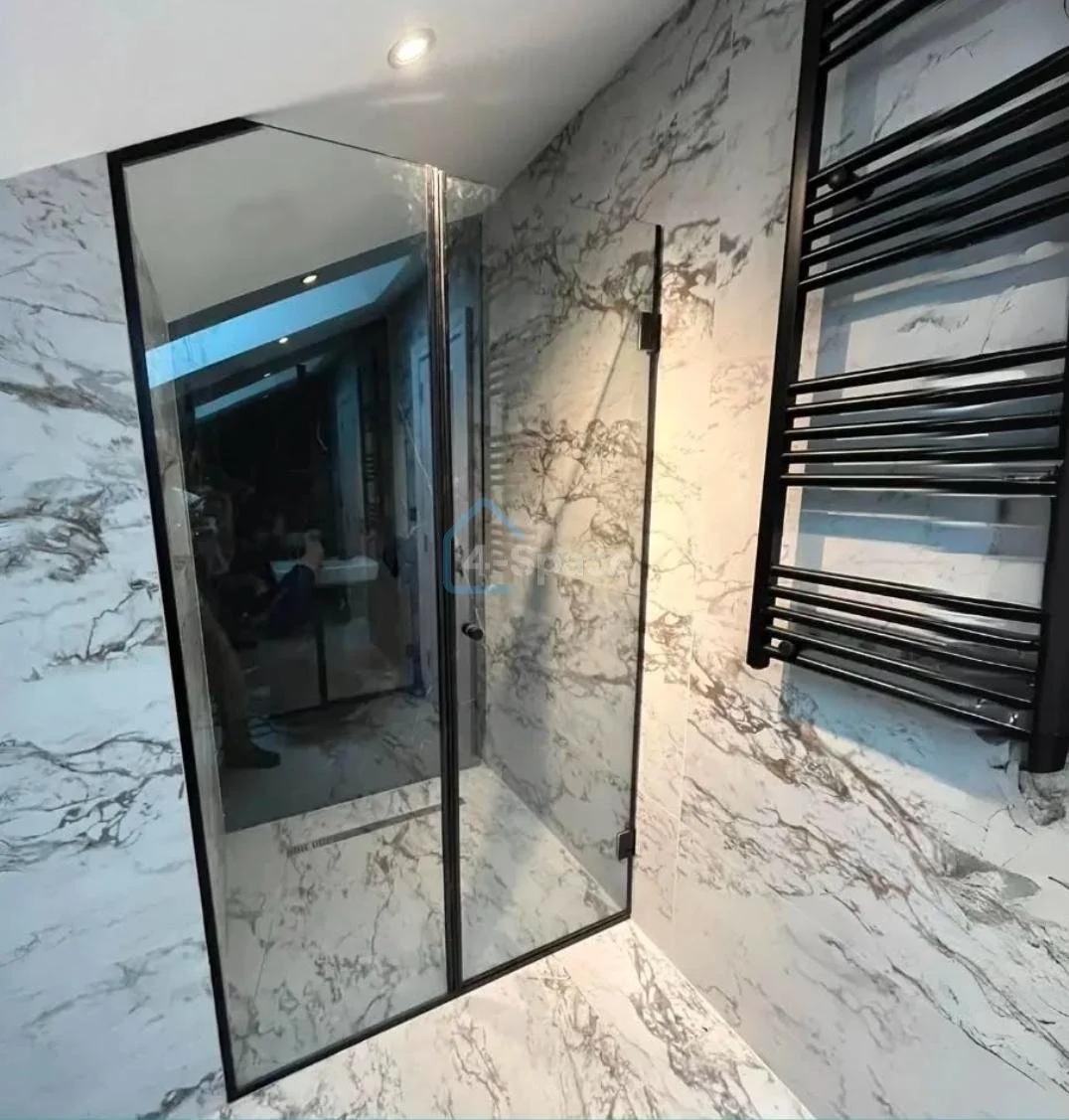 Modern bathroom with marble walls and floor, a glass shower door, and a black heated towel rack mounted on the wall.