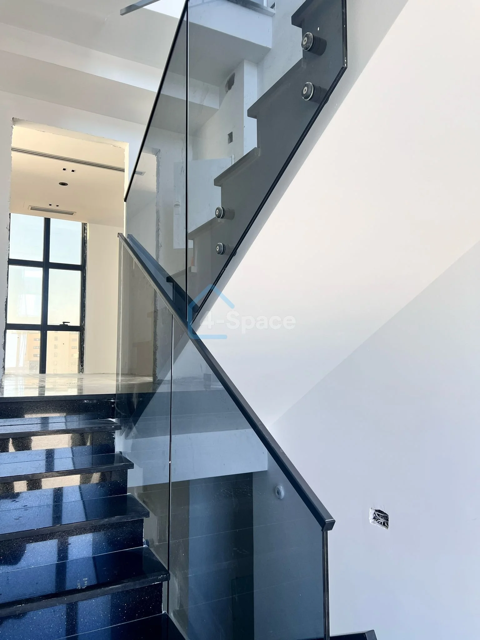 Modern staircase with black steps and a glass railing inside a building with white walls and a large window.