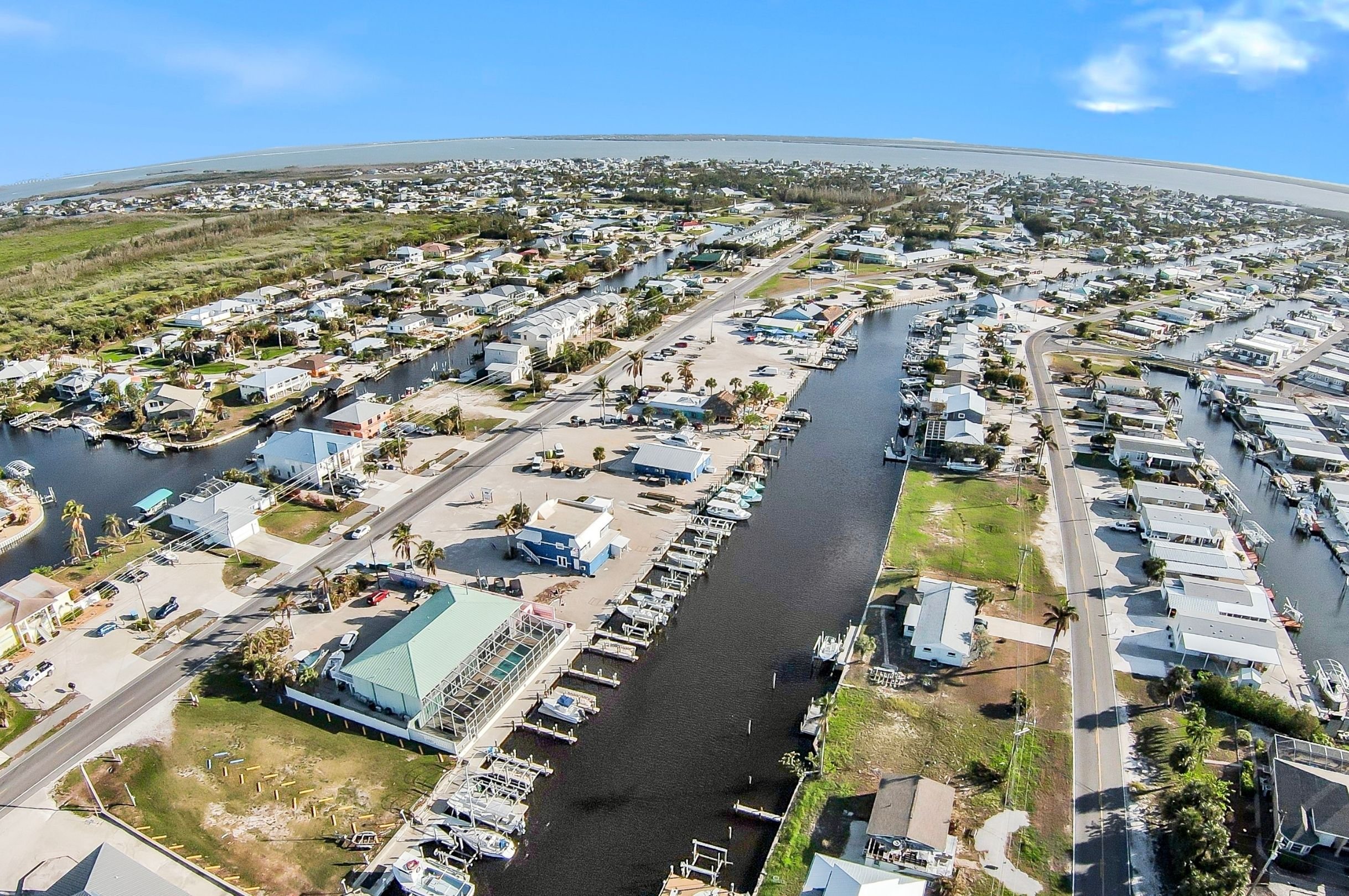 Aerial view of a coastal residential area with houses, boats, and waterways under a partly cloudy sky.