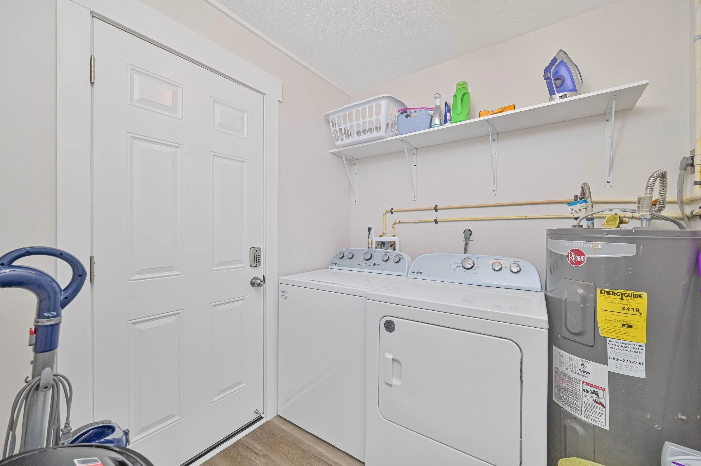 Laundry room with a white door, a washing machine, a dryer, a water heater, and a white shelf holding laundry supplies.
