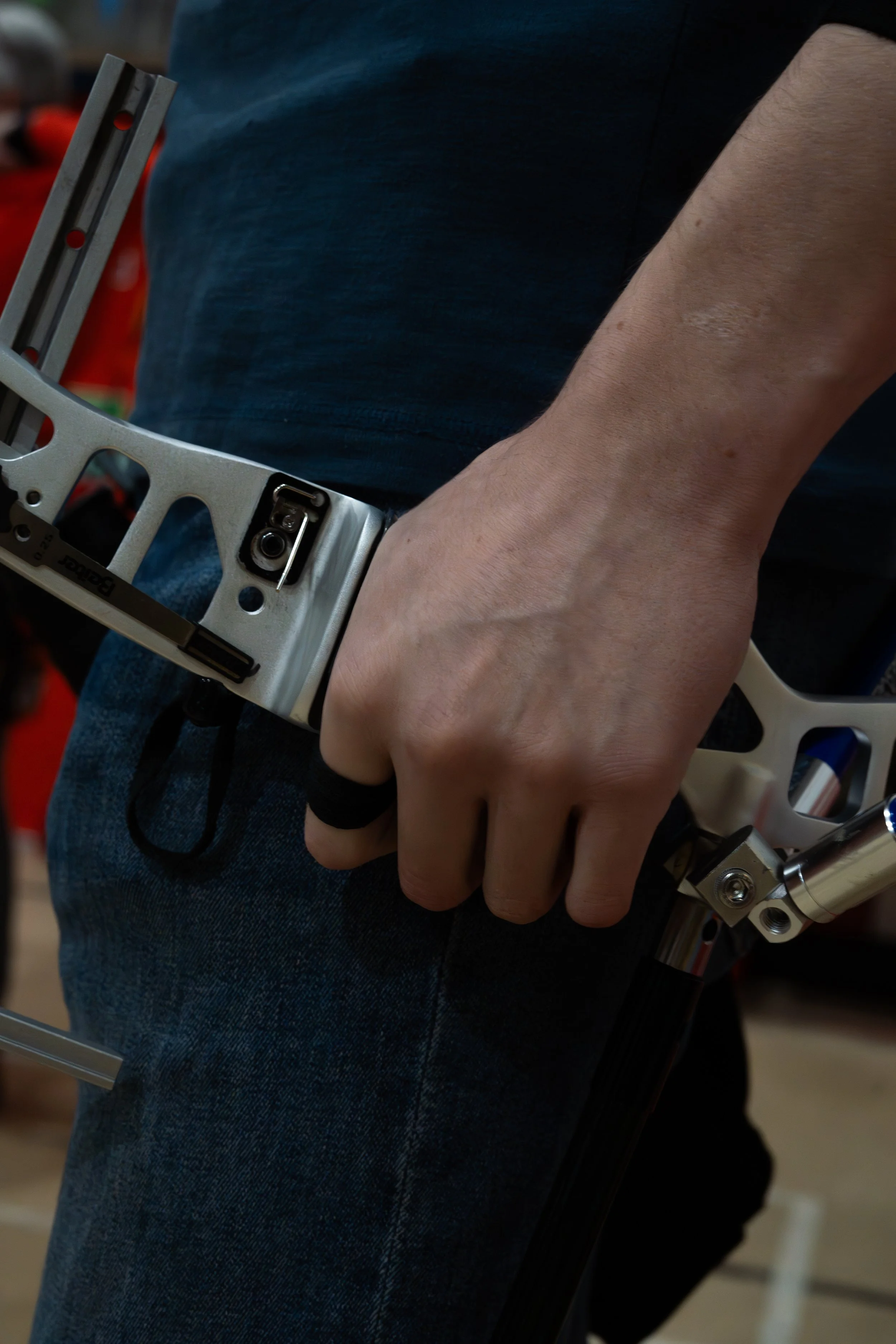Close-up of a person's hand holding a metallic skateboard truck, with part of the skateboard deck and the person's blue jeans visible.