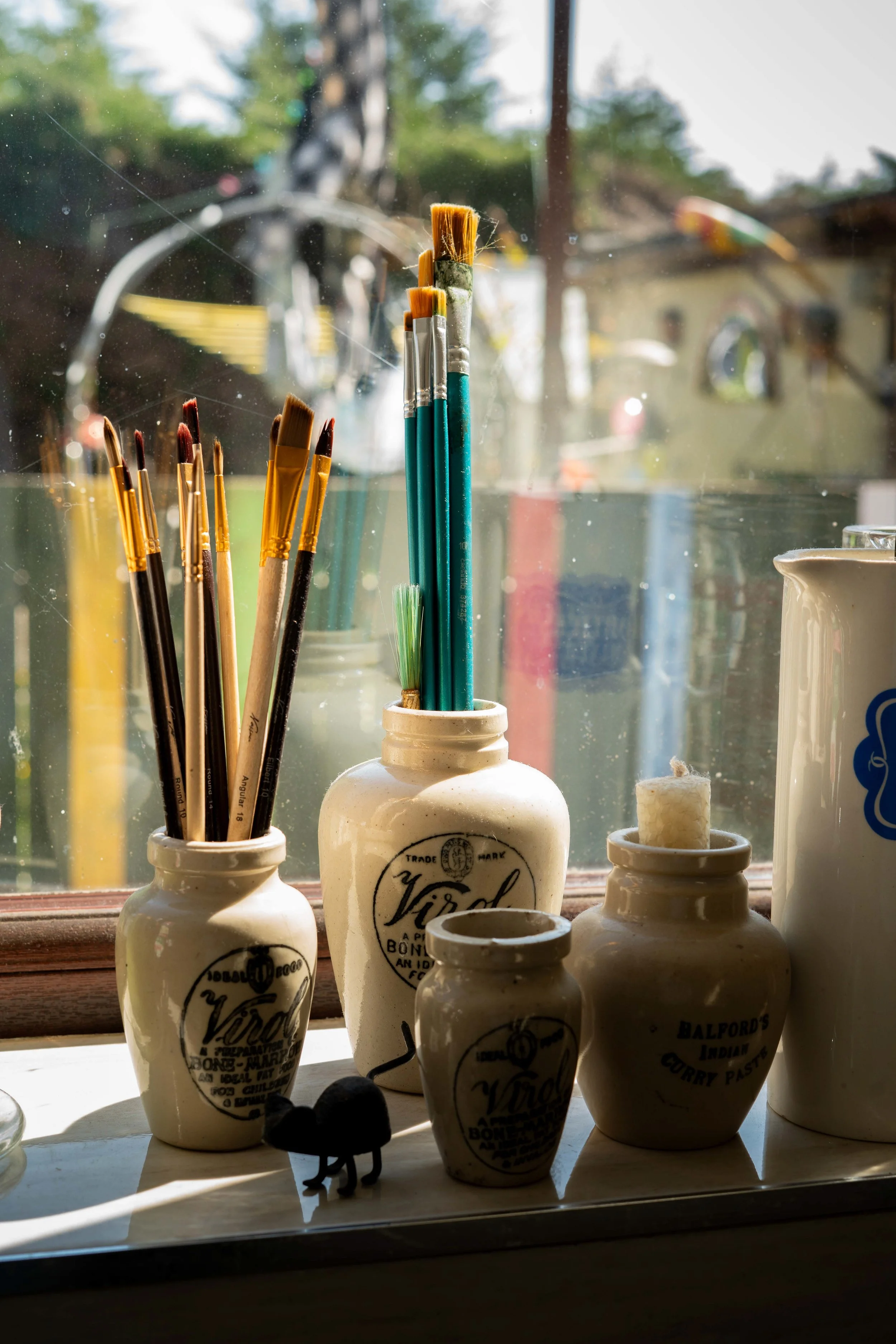 Paintbrushes and art supplies in ceramic jars on a windowsill.