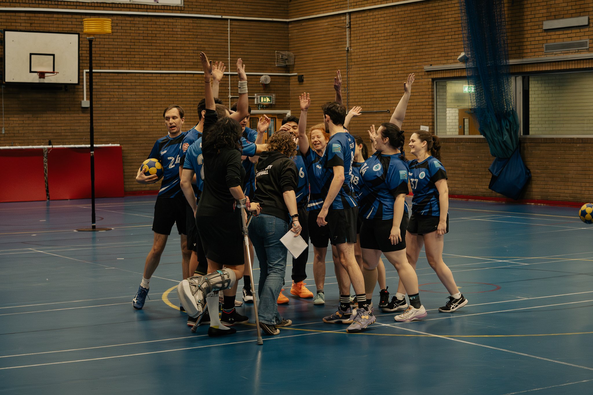 A group of volleyball players in blue jerseys celebrating together on an indoor court, with some raising their hands for high fives.