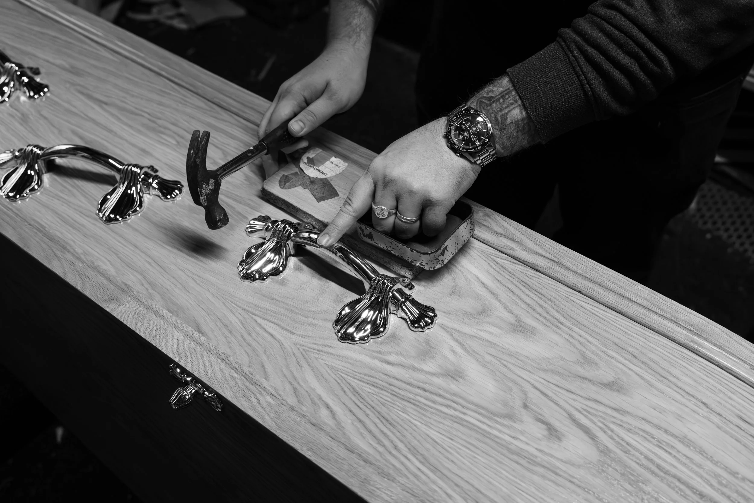 A person working with jewelry on a wooden table, using a hammer and tools, with shiny, flower-shaped metallic pieces on display.
