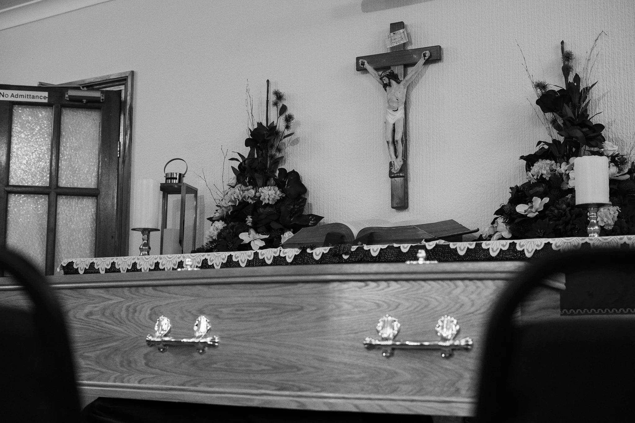 An altar in a church with a crucifix, flowers, a Bible, and candles, shot in black and white.
