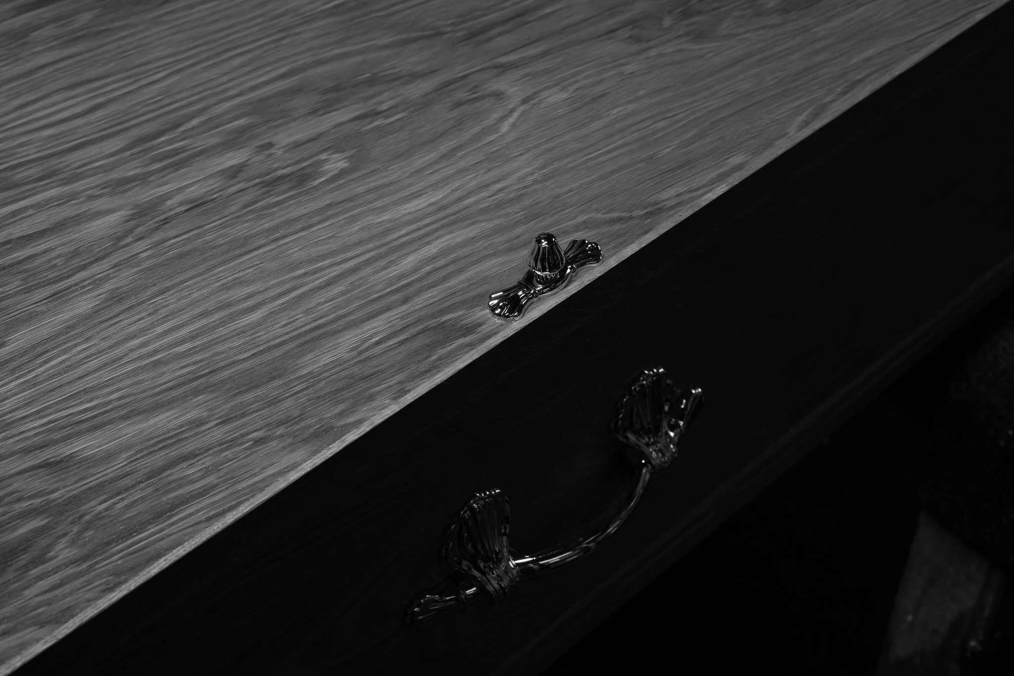 Close-up of a drawer handle shaped like a bow, attached to a piece of furniture with a wood grain finish. The image is in black and white.