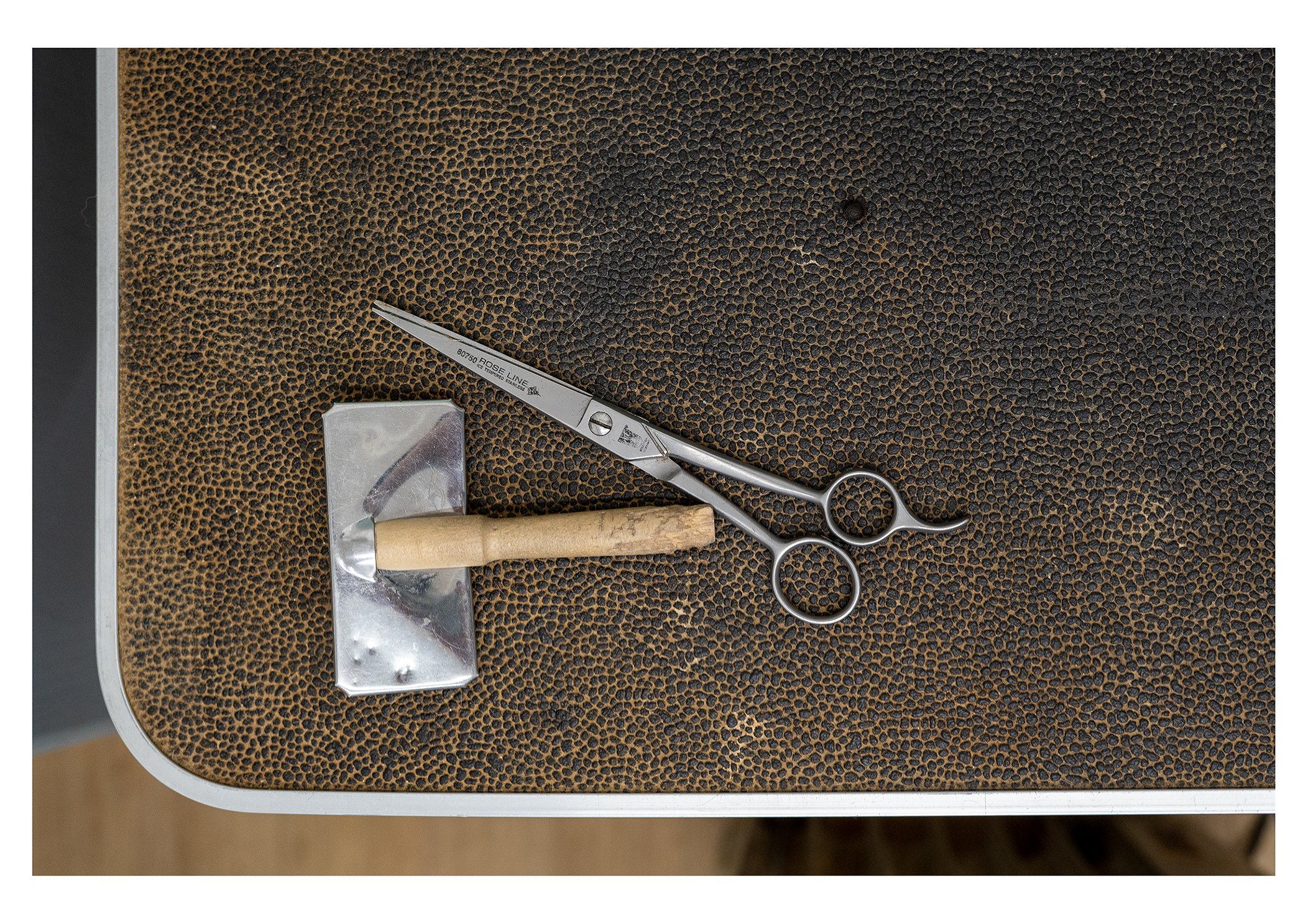 Surgical scissors, a small medical instrument, and a spool of suture with a needle on a textured brown surface.