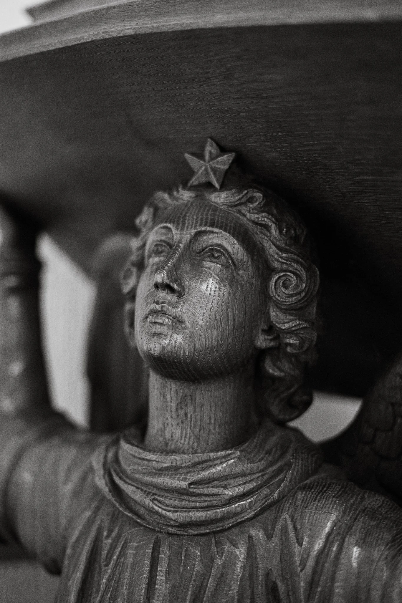 Black and white photo of a carved wooden sculpture of a woman with a star on her forehead, holding a large object above her head.