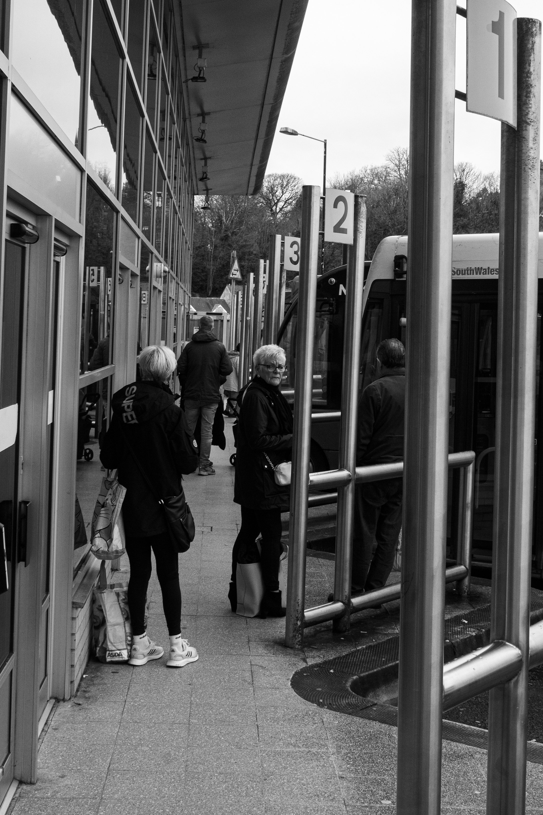 People standing in line at a bus stop with numbered signs, and a bus arriving.
