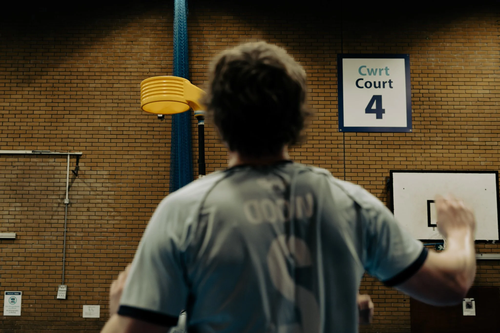 A person playing basketball indoors at CWRT Court 4, with a basketball hoop and a yellow wall-mounted device in the background.