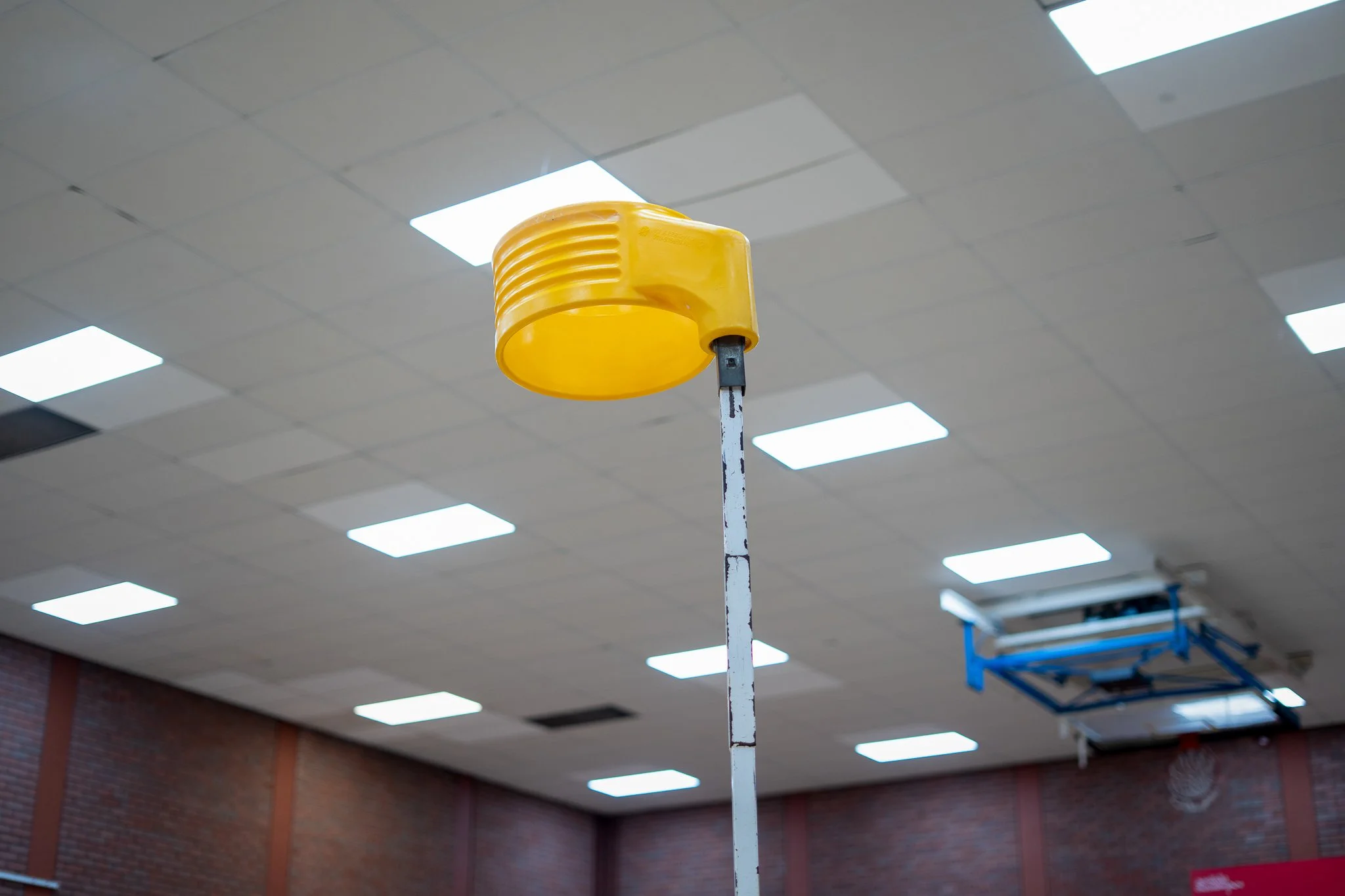A yellow caution or warning light mounted on a tall metal pole in an indoor setting with a grid ceiling and bright overhead lights.