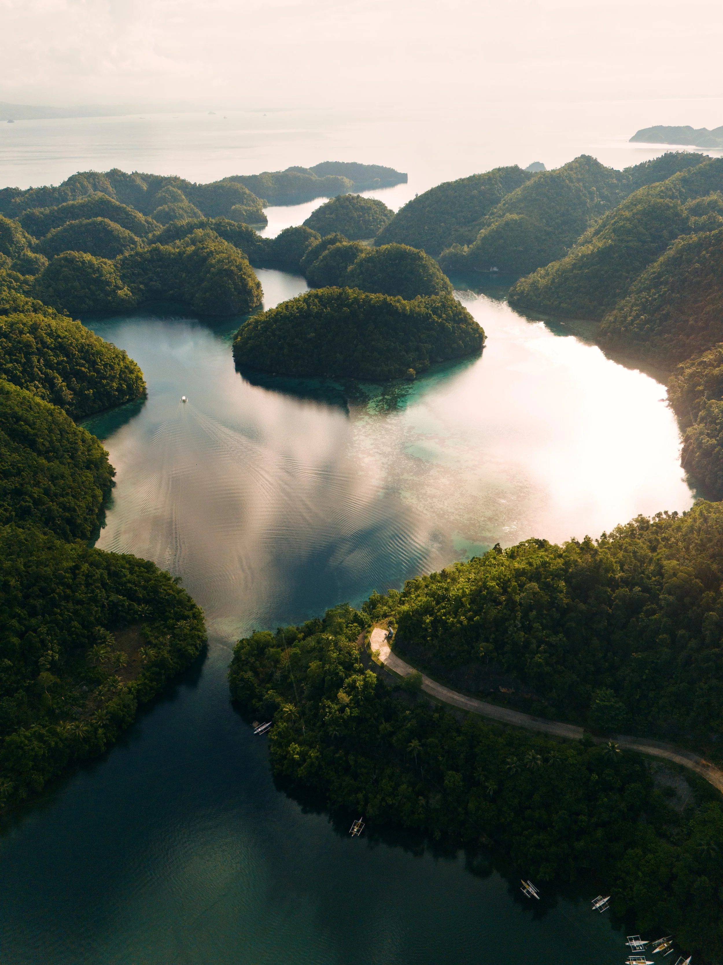 Aerial view of a river with numerous green islands, surrounded by dense forest, with boats on the water and a road winding through the trees.