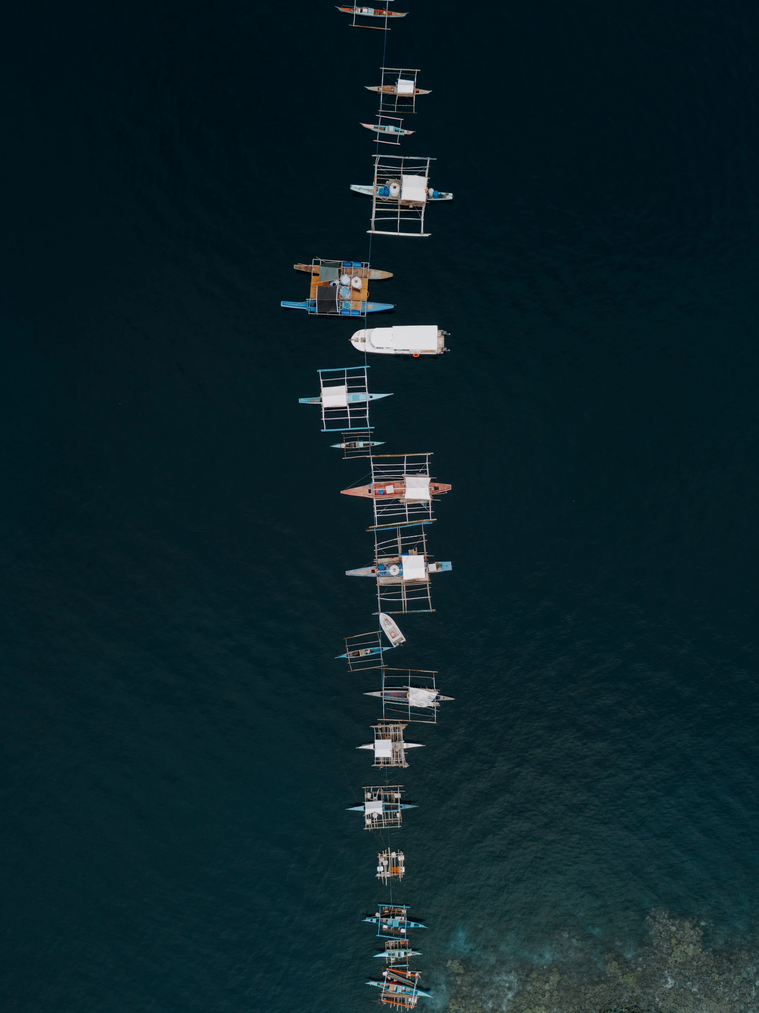 Aerial view of boats anchored in a straight line on dark blue water.