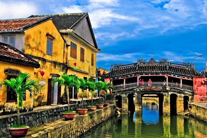 Colorful old buildings with potted plants and a bridge over a canal in a scenic town.