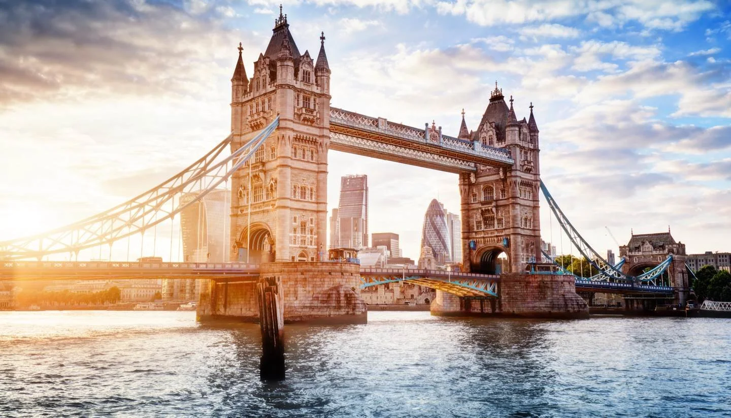 London's Tower Bridge over the River Thames at sunset with modern city skyscrapers in the background.