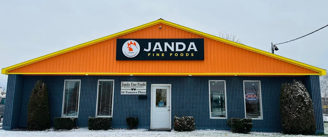 Front view of Janda Fine Foods store with a blue exterior, yellow gable, and sign reading 'Janda Fine Foods' with a logo, in a snowy setting.