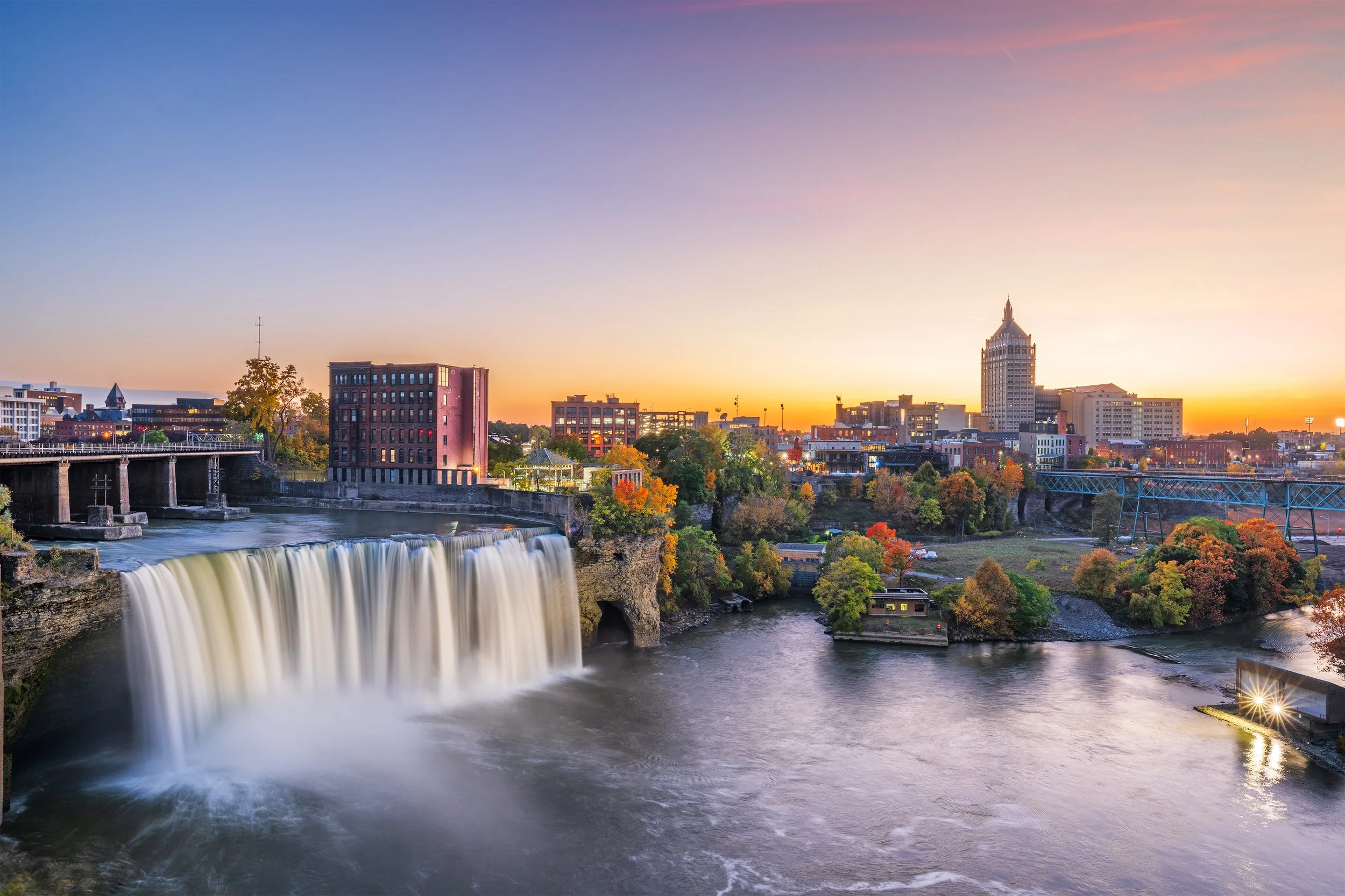 City skyline at sunset with waterfall in the foreground.