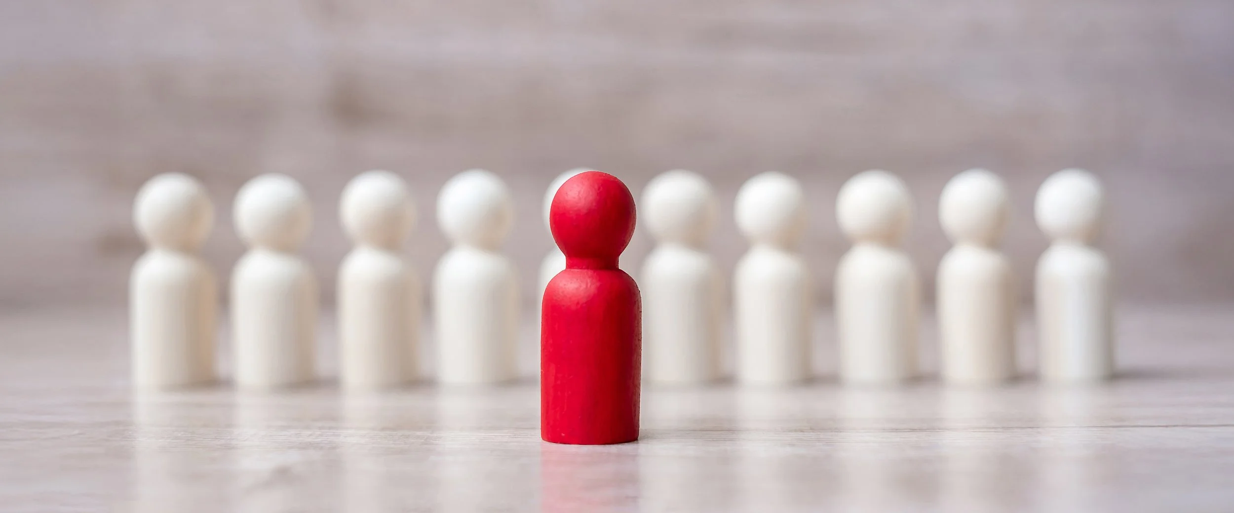 Red game piece in front of a row of white game pieces on a wooden surface with blurred background.