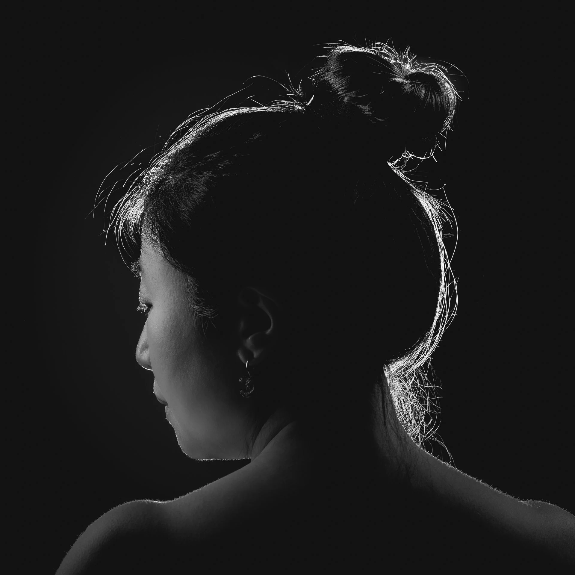 A silhouette of a woman with her hair styled in an elegant updo, highlighted by backlighting that accentuates her profile and hair details against a dark background.
