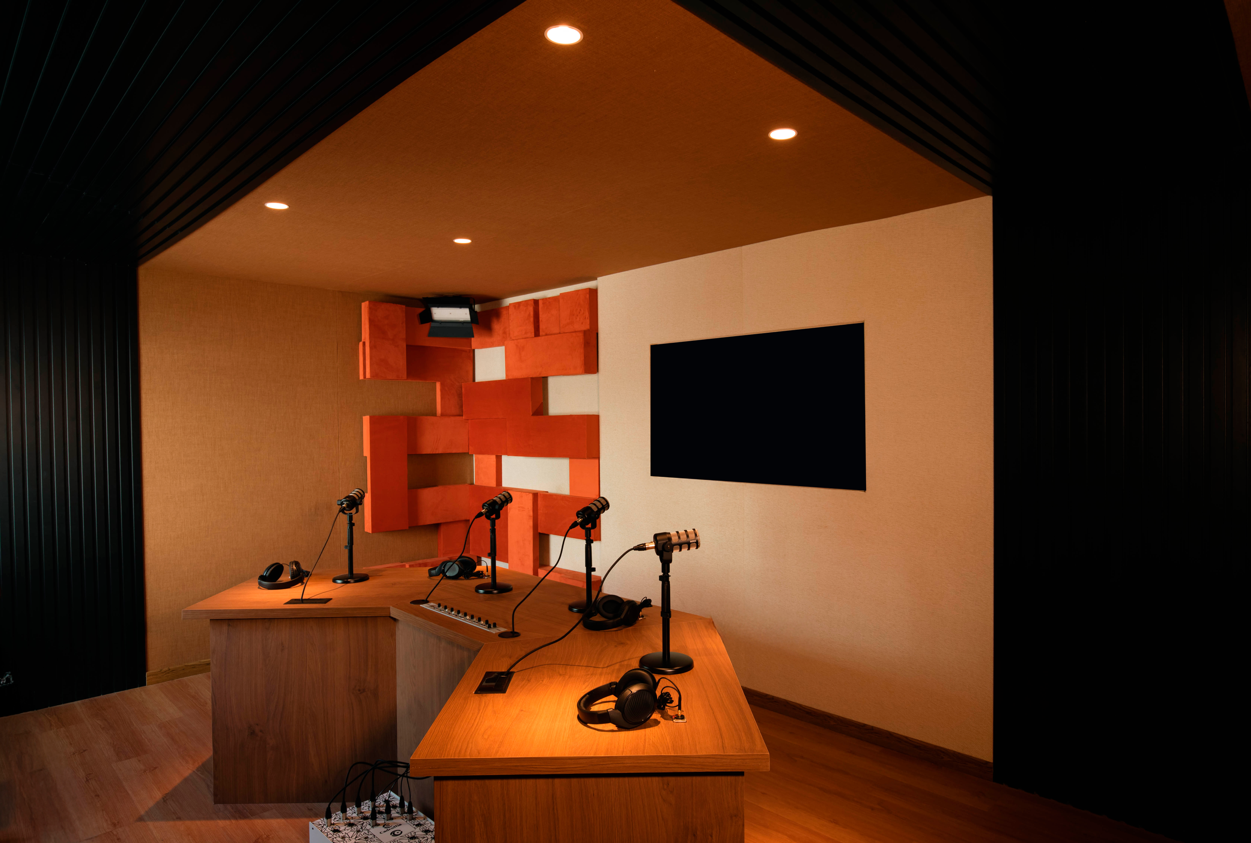 Estudio de grabación con mesa de mezclas, micrófonos, auriculares y pantalla en la pared.