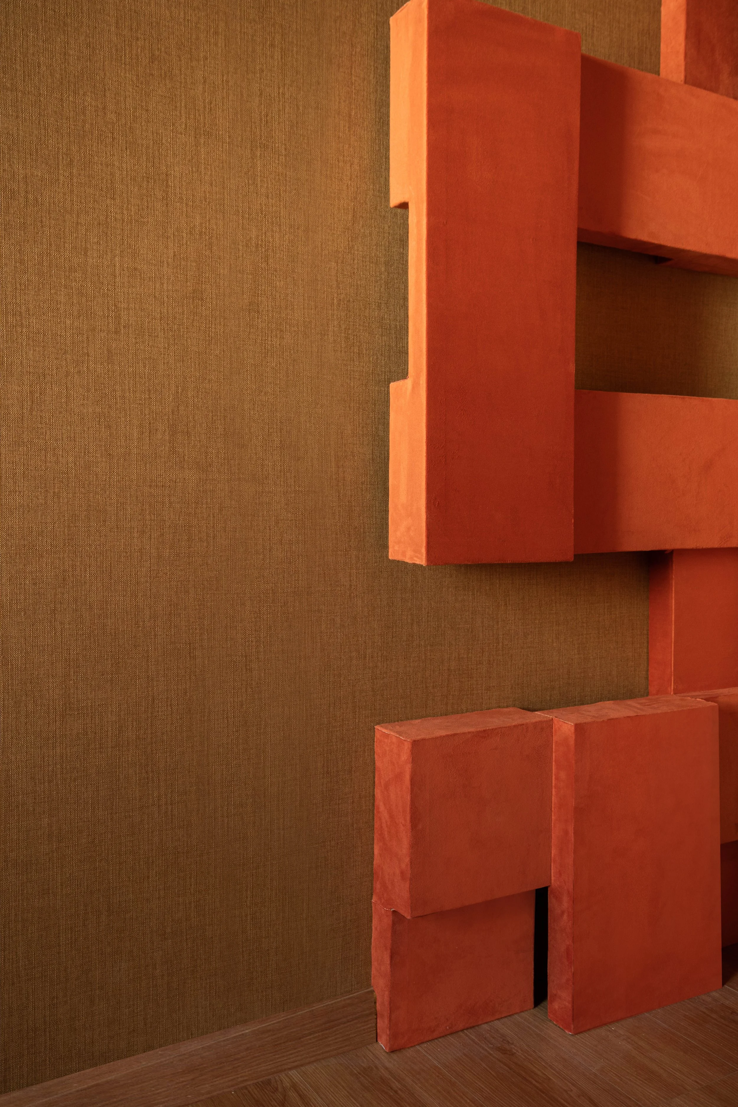 Block de madera pintado de color rojo colocados en el suelo y en la pared de un cuarto con pared color marrón y piso de madera.