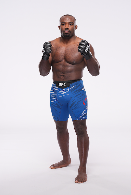 Mixed martial artist in blue fight shorts and UFC gloves standing in a fighting stance against a white background.