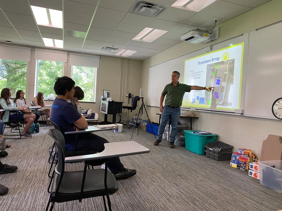 Eric Beck pointing to solar powerpoint while students sit at desks and listen.