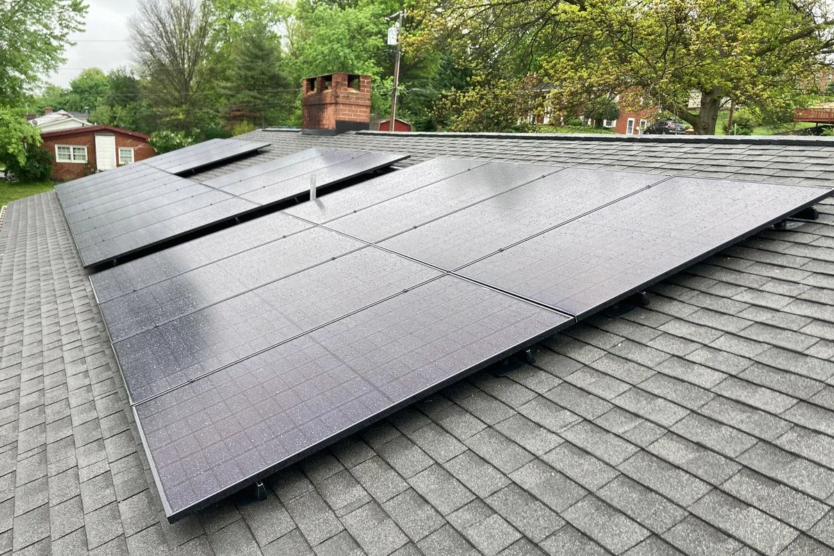 Solar panels installed on a residential roof with trees and neighboring houses in the background.