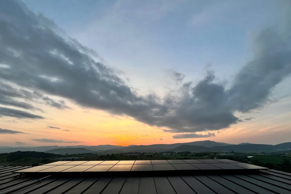 Solar panels on a metal roof with a sunset and cloudy sky in the background.