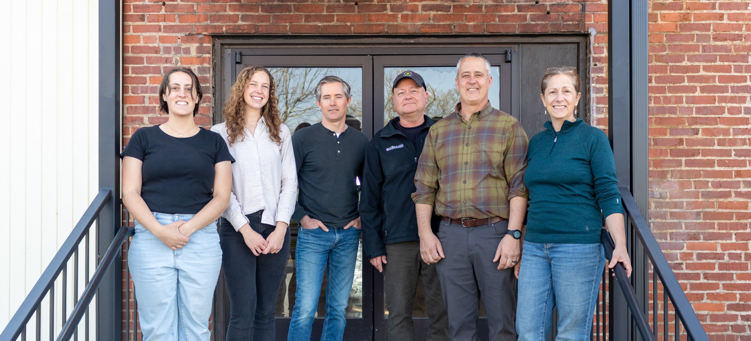Six people on the Green Hill Solar team standing outside in front of a glass door and brick building, smiling at the camera.
