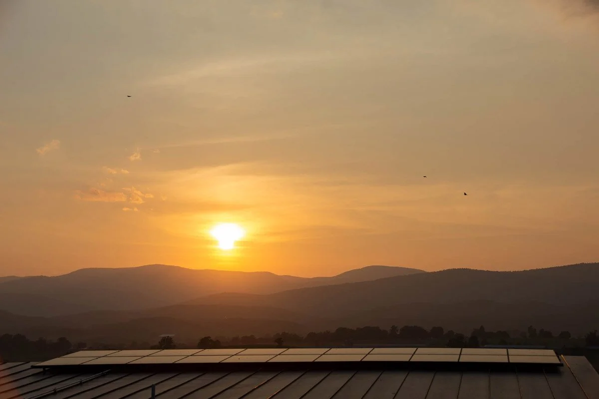 Sunset over mountains with a solar panel in the foreground and birds flying in the sky.