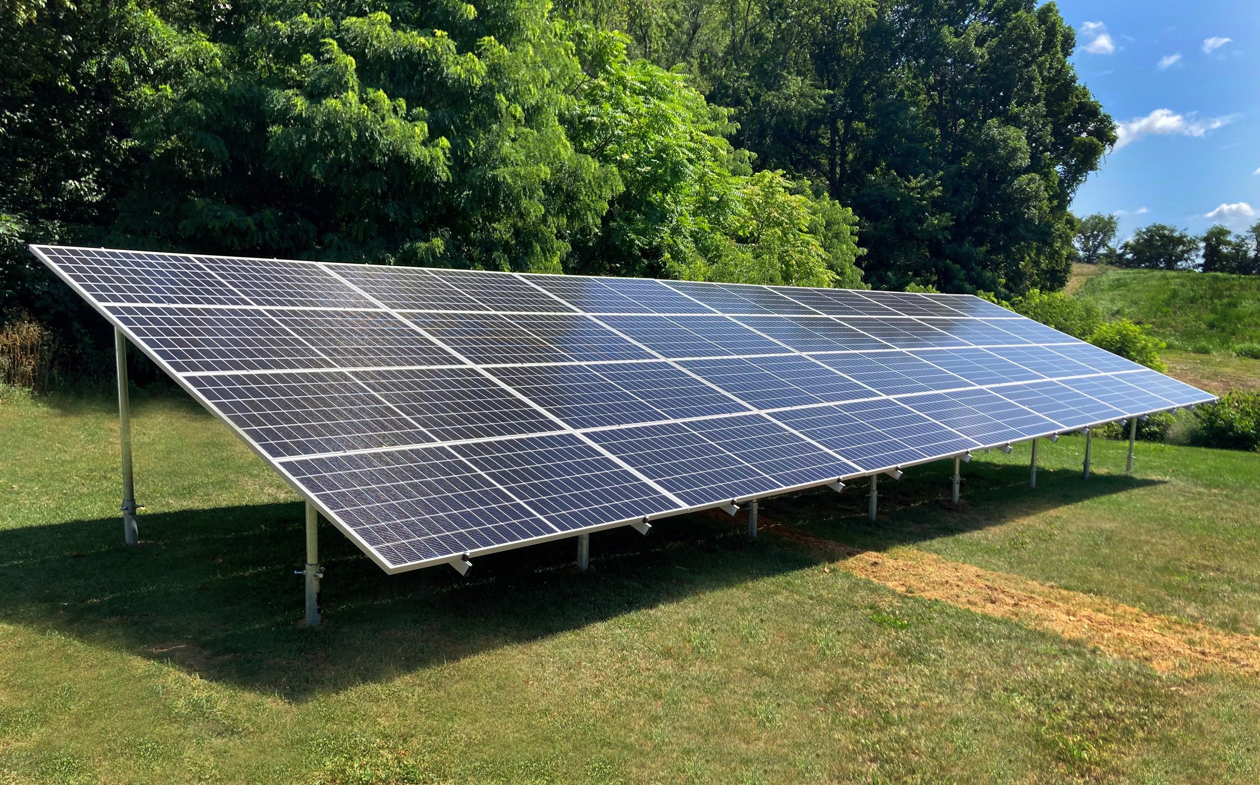 Ground-mounted solar panels installed on a grassy field with trees and blue sky in the background