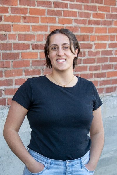 Asha Landes Beck portrait in front of brick wall.