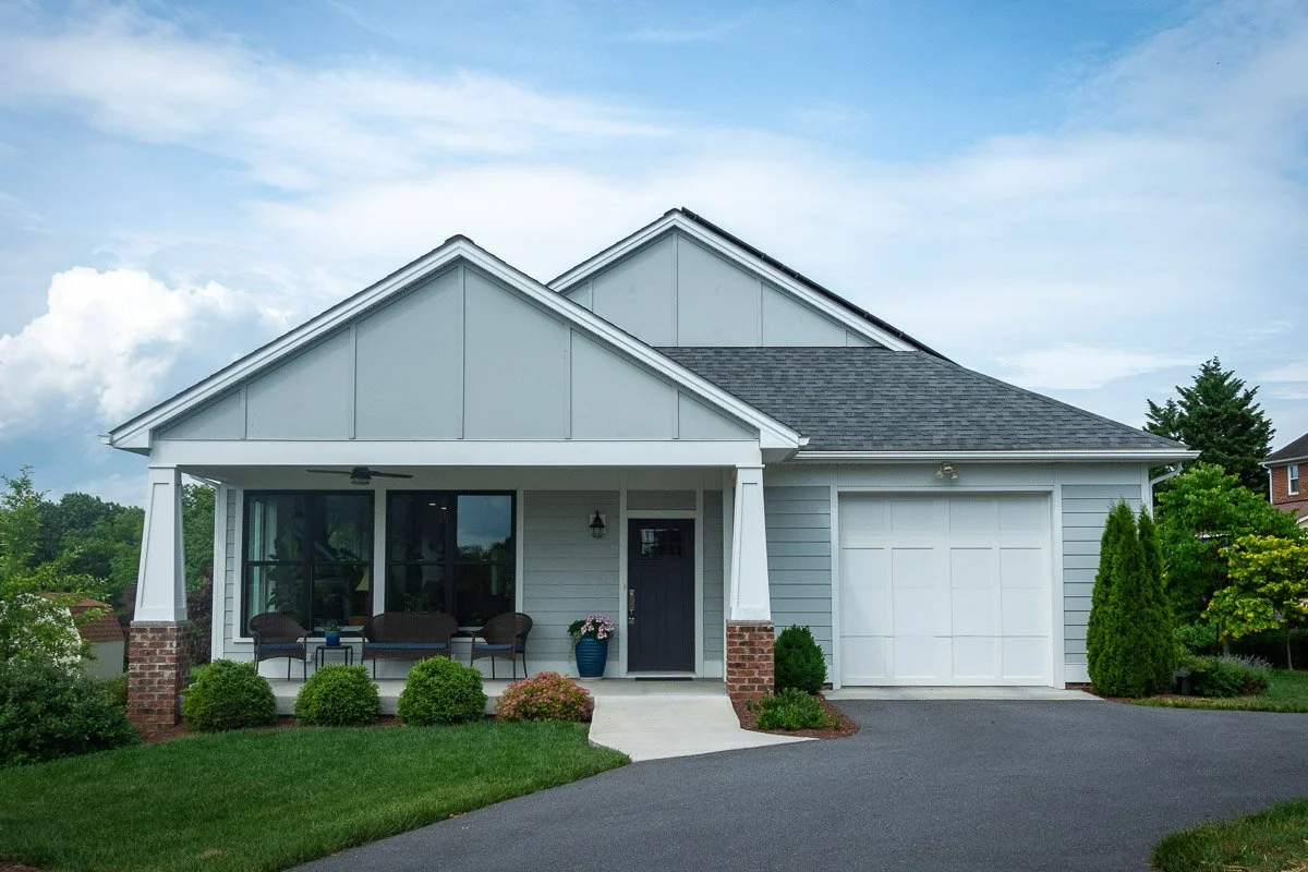 Front view of a modern white house with a small front porch, black door, large window, attached garage, and well-maintained garden with shrubs and a lawn.