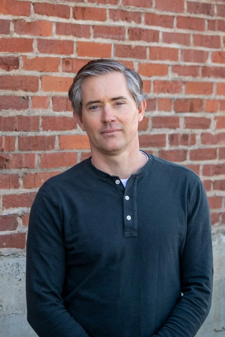 Tim Nelson portrait in front of brick wall.
