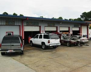 A parking lot in front of a building with three garage doors, with several parked vehicles including SUVs and sedans.