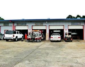 Auto repair shop with four garage bays, four cars in front, and tools visible inside the bays.