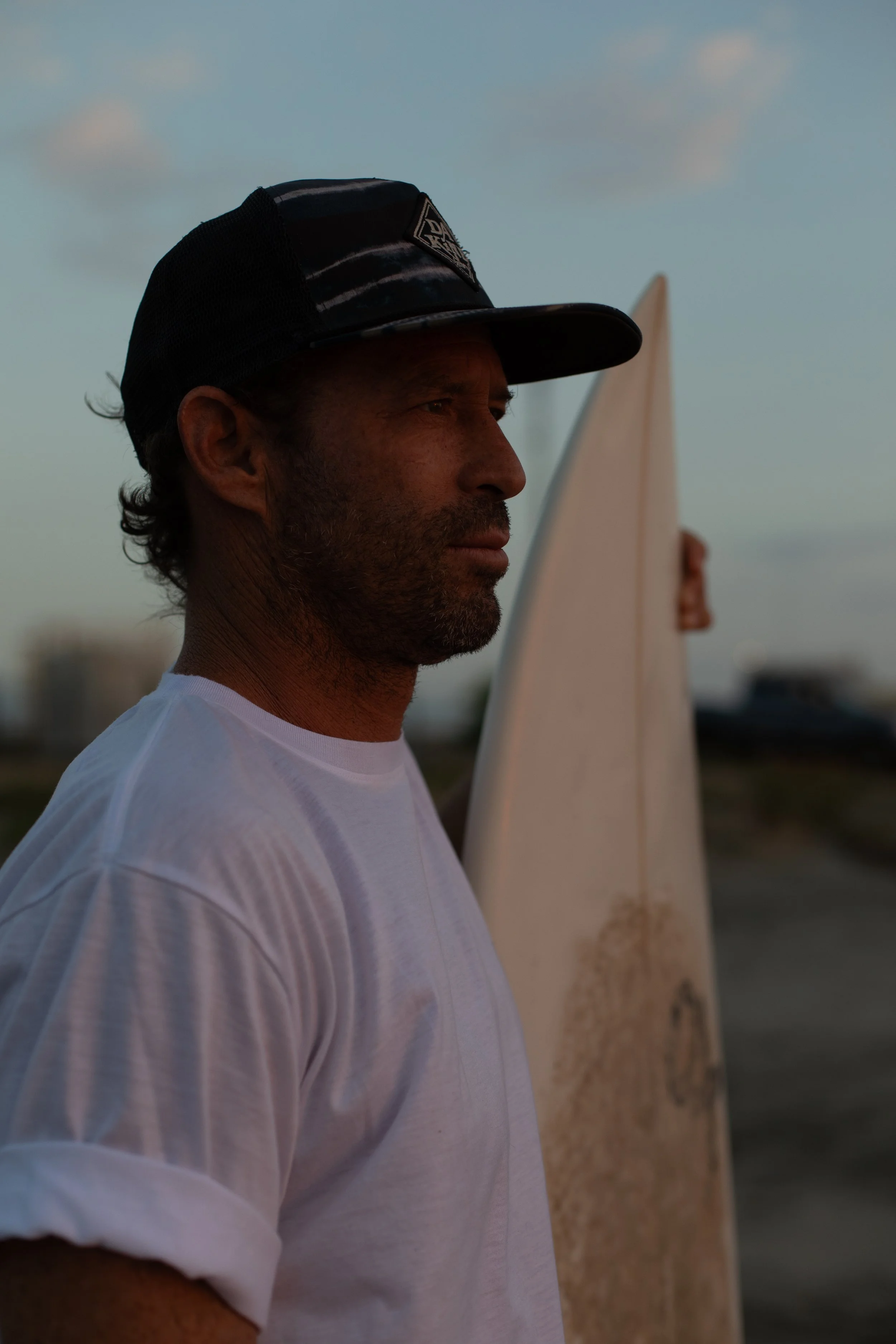 Man walking on beach with other people nearby, rocks in the background, black and white photograph.