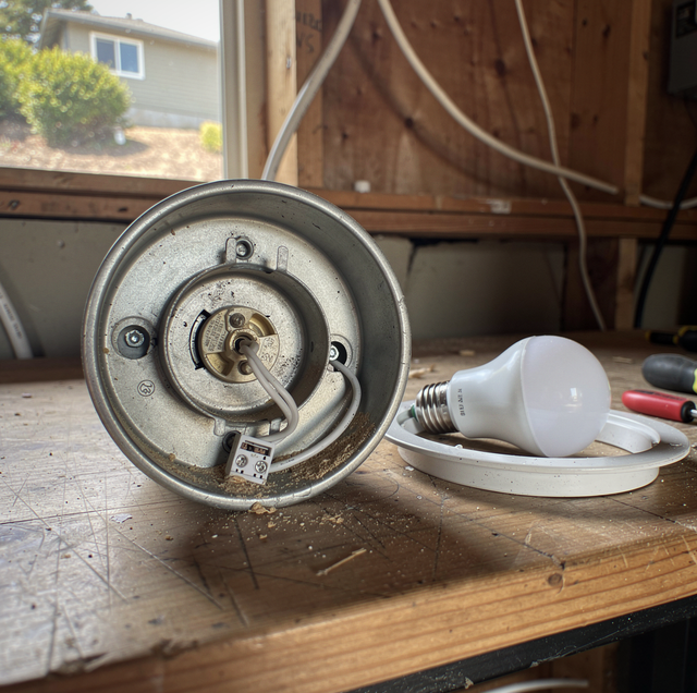 Disassembled light fixture with metal base and socket next to a white LED bulb on a wooden surface.